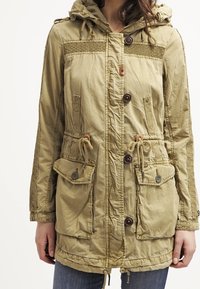 Parka kaki avec capuche, corsage texturé et deux poches avant. Comprend une taille à cordon de serrage et des fermetures par boutons.
