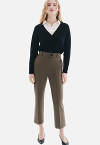 Cardigan marine à décolleté en V et fermeture à boutons, associé à un pantalon olive ajusté. Des escarpins noirs complètent la tenue.