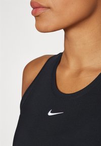 Black athletic tank top with a round neckline, featuring a white Nike logo on the chest and textured knit fabric. Close-up view.