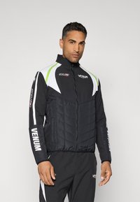 Black padded jacket featuring white and green accents, high collar, and VENUM branding. Quilted texture and zip closure.