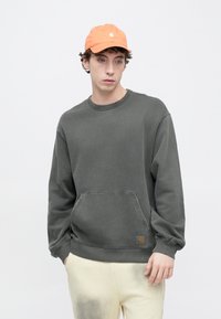 Felpa grigia con tasca frontale, polsini e collo a costine. Abbinate a un berretto arancione con logo. Tessuto morbido, vestibilità comoda.