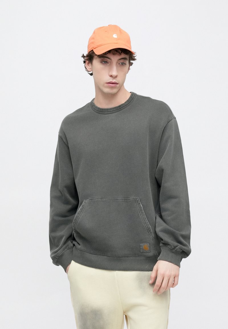 Grå sweatshirt med framficka, ribbade mudd och krage. Kombinerad med en orange keps med en logotyp. Mjukt tyg, avslappnad passform.