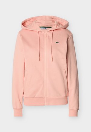 Ανοιχτό ροζ φούτερ με φερμουάρ, εμπρόσθιες τσέπες, κορδόνια, ριμπ μανσέτες και τελείωμα, καθώς και μικρό πράσινο λογότυπο κροκοδείλου στο αριστερό στήθος.