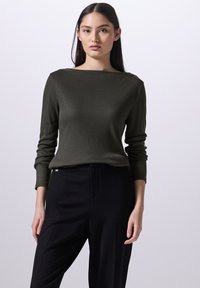 Olivgrünes, geripptes Langarm-Oberteil mit einer Boot-Ausschnitt, kombiniert mit hoch sitzenden schwarzen Hosen. Einfaches Design, glatte Textur, taillierte Form.