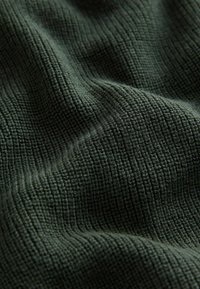 Tissu vert texturé avec un design à canelures, présentant une apparence tissée douce et des profondeurs variées à la surface du matériau.