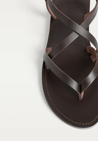 Brun læder sandal med krydsende remme, en glat indersål og detaljeret syning langs kanterne. Minimalistisk design.