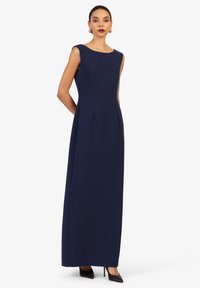 Donkerblauwe mouwloze maxi-jurk met een ronde hals, zijzakken, rechte silhouette en een gladde stof. G gedragen met zwarte hakken.