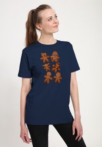 T-shirt bleu marine avec huit motifs de biscuits en pain d'épice en marron et orange, chacun présentant des caractéristiques faciales et des décorations distinctes.
