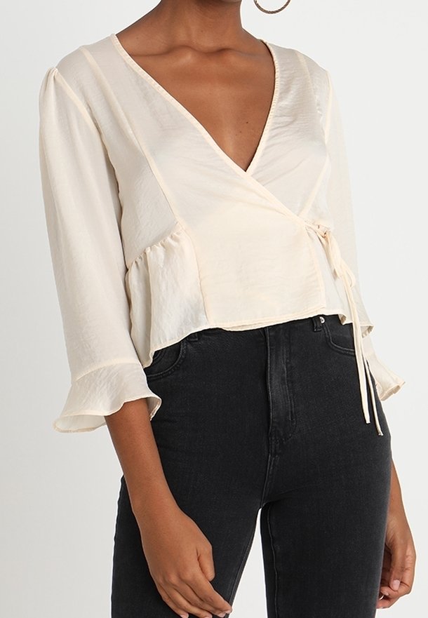 Krämfärgad omslagblus med trekvartslånga ärmar, rynkiga manschetter och knyt vid midjan, tillverkad av ett mjukt, lätt tyg.