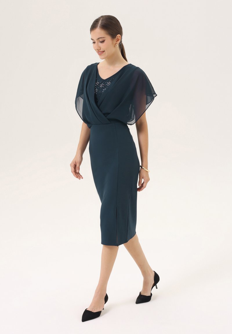 Turquoise jurk met doorschijnende kapmouwen, V-hals, versieringen op de borst en een aansluitende snit met een knie-lange zoom en een zijsplit.