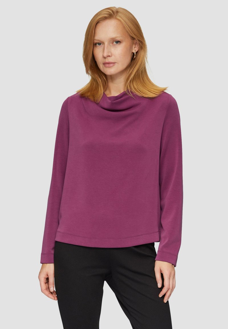 Violetti cowl-kaula pitkähiha paita pehmeästä kankaasta, jossa on rento istuvuus ja suora helma, yhdistettynä mustiin housuihin.