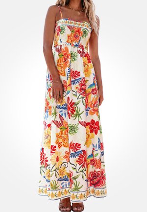 Mujer con un vestido blanco sin mangas hasta el suelo, con patrones vibrantes de flores y pájaros en rojo, naranja, amarillo y verde, combinado con sandalias marrones.