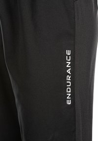 Mustat urheiluhaalari, joka on valmistettu sileästä ja hengittävästä kankaasta. Sivussa on valkoinen "ENDURANCE"-logo ja slim fit -design.