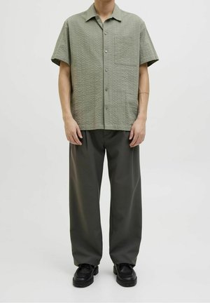 Camicia a maniche corte di un verde chiaro texturizzato con taschino, abbinata a pantaloni larghi di un verde scuro e scarpe con plateau nere.