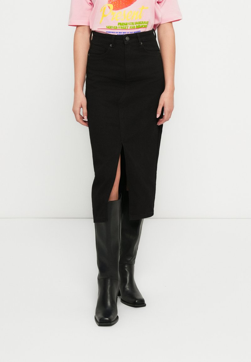 Melna džinsa midi svārki ar priekšējā šķēluma, pieguļošu vidukli un taisnu griezumu. Valkāti kopā ar melniem zābakiem līdz ceļiem.