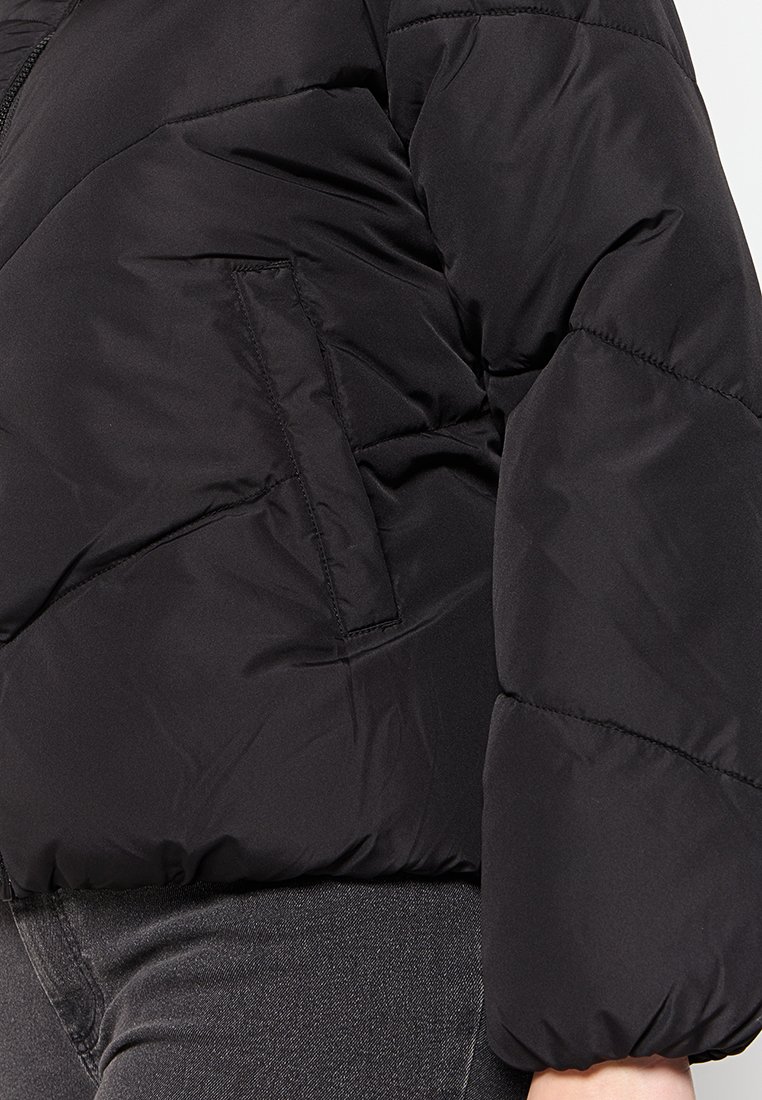 Giubbotto puffer nero con design trapuntato, dotato di chiusura con zip e tasca laterale. Il tessuto sembra liscio e leggermente lucido.