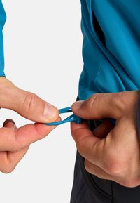 Giacca impermeabile blu con un primo piano di mani che regolano il cordino. Caratteristiche includono un tessuto morbido e un colore di accento contrastante.