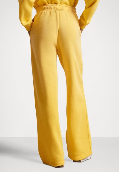 Gule joggebukser laget av mykt stoff, med elastisk midjebånd, sidelommer og en avslappet passform som smalner ned mot bunnen.