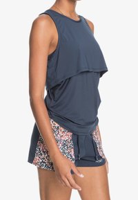 Marinblå atletisk linne med lagerdesign och strukturerad tyg; kombinerat med shorts med blommönster och dragsko.