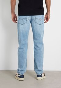 Jeans in denim blu chiaro con taglio dritto, dotati di due tasche posteriori e un piccolo pannello con logo. Abbinati a scarpe scure.