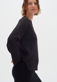 Maglia nera a maniche lunghe in tessuto morbido, con una vestibilità rilassata e scollo rotondo, indossata con una gonna nera testurizzata.