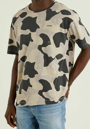 T-shirt beige avec un grand motif de vache noire. Fabriqué en tissu doux, il présente un col rond, des manches courtes et un logo de marque discret.