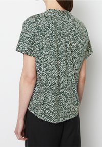 Top verde a maniche corte con un motivo astratto bianco, caratterizzato da un taglio comodo e dettagli plissettati sul retro. Tessuto dalla texture liscia.