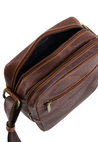 Bruine leren crossbodytas met meerdere ritssluitingen, een gestructureerd oppervlak en verstelbare riem. Voorzien van een subtiel logo en messing accenten.