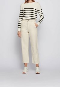 Pantalon large couleur crème, taille haute avec poches avant, associé à un haut à manches longues rayé noir et blanc. Baskets blanches.