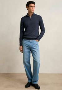 Marineblaues Zip-Hals-Sweatshirt im lässigen Schnitt, kombiniert mit hellblauen, schmal geschnittenen Jeans und schwarzen Schuhen. Glatte Textur, schlichtes Design und funktionale Details.