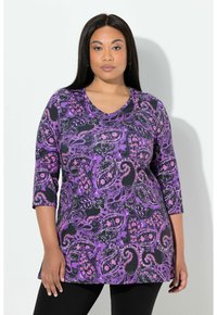 Fioletowa bluzka z wzorem paisley, z rękawami do połowy przedramienia i dekoltem w kształcie litery V, zestawiona z czarnymi legginsami. Materiał wygląda na miękki i teksturowany.