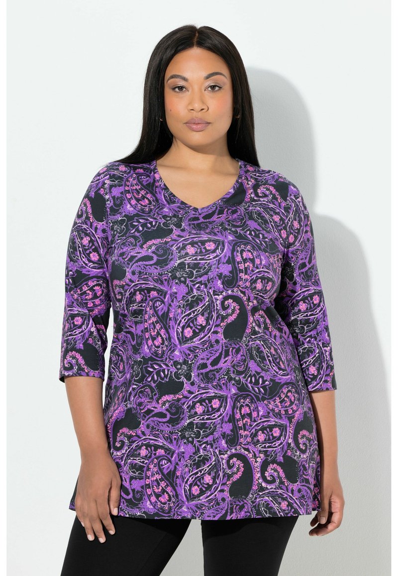 Fioletowa bluzka z wzorem paisley, z rękawami do połowy przedramienia i dekoltem w kształcie litery V, zestawiona z czarnymi legginsami. Materiał wygląda na miękki i teksturowany.
