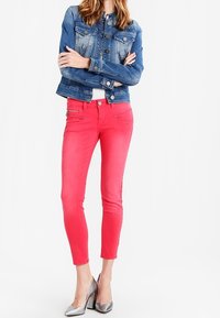 Růžové úzké džíny s mírným leskem a zipy na předních kapsách, doplněné modrou džínovou bundou. Celý outfit doplňují stříbrné lodičky na vysokém podpatku.