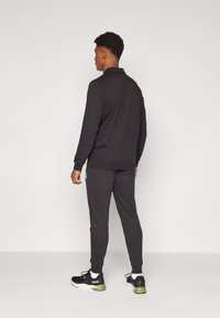 Donkergrijze sporthoodie met een kraag, bijpassende joggers en zwarte sneakers met groene accenten. Eenvoudige, gestructureerde stof met ribgebreide boorden.