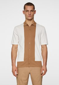 Polo a maniche corte con un design a blocchi di colore marrone e bianco. Tessuto morbido, frontale con bottoni e colletto.