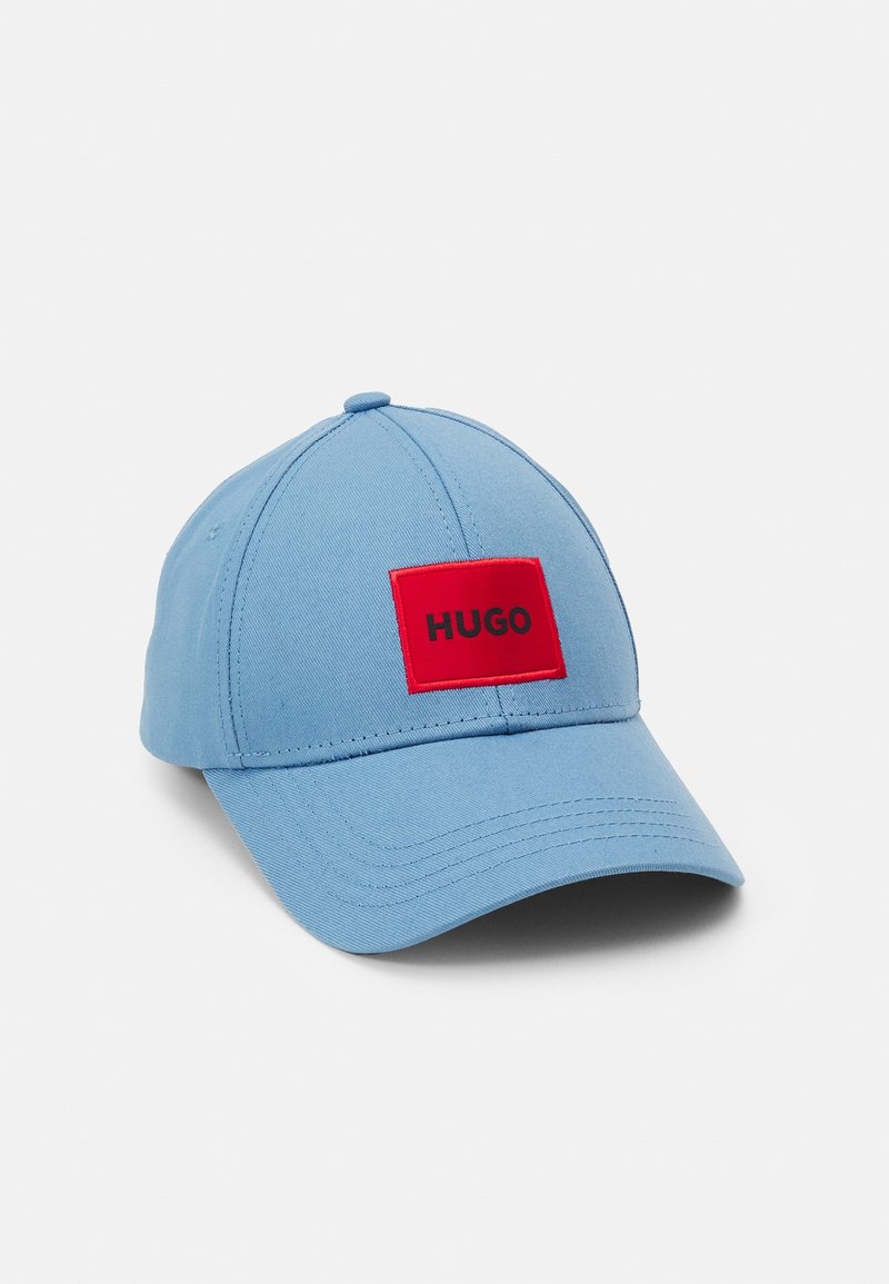 Casquette de baseball bleu clair avec un patch rectangulaire rouge affichant le mot « HUGO » en texte noir sur le panneau avant.