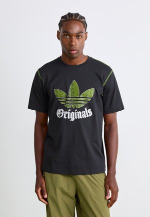 Black cotton t-shirt featuring a distressed green Adidas trefoil logo and white "Originals" text, with green accent stitching on shoulders.
