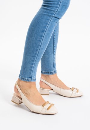 Scarpine beige con punta tonda, finitura lucida, cinturini decorativi marroni e tacco a blocco testurizzato. Indossate con jeans skinny blu.