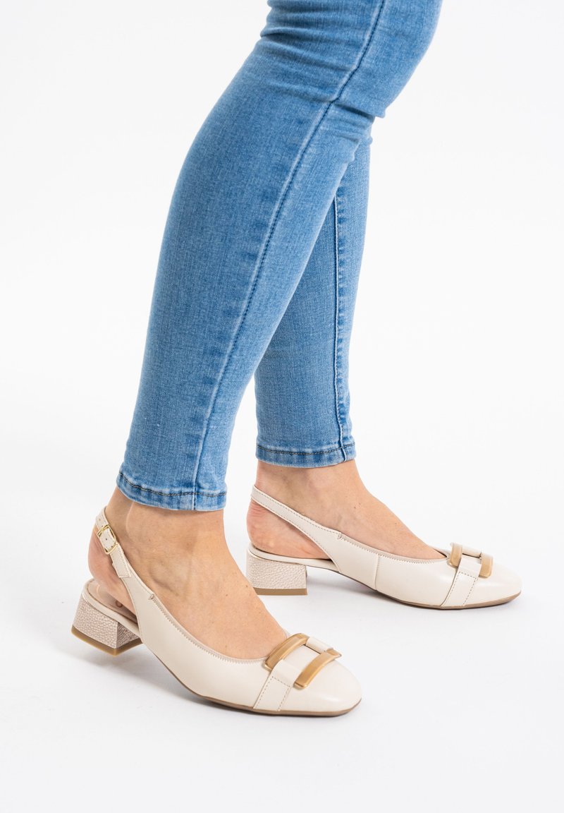 Scarpine beige con punta tonda, finitura lucida, cinturini decorativi marroni e tacco a blocco testurizzato. Indossate con jeans skinny blu.