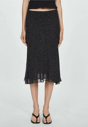 Zwarte midirok met witte polka dots, lichte uitlopende zoom, gedragen door een persoon in combinatie met zwarte teenslippers.