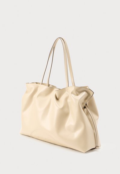 Grand sac fourre-tout en cuir souple beige avec deux fines bretelles, texture légèrement froissée et design simple.