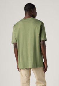 T-shirt in cotone verde oliva con maniche corte, colletto rotondo e vestibilità rilassata, caratterizzato da una texture liscia e morbida e un design minimalista.