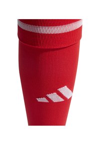 Calcetín deportivo rojo con textura acanalada, rayas blancas en la parte superior y diseños geométricos en blanco cerca del tobillo.