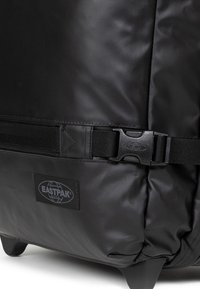 Černý batoh Eastpak vyrobený z odolného, texturovaného materiálu; má plastovou sponu a odznak s logem. Tvar je obdélníkový s zaoblenými okraji.