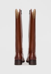 Brown leather knee-high boots with a rounded toe, smooth texture, back zipper, and a stacked heel, featuring a distinct top cutout design.