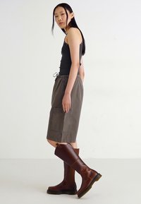 Black tank top, gray drawstring skirt with pockets, and tall brown leather boots, featuring a smooth texture and sleek design.