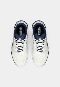Pantofi sport albi cu un interior texturat de culoare bleumarin și șireturi albe; au un logo pe limbă și linii de design distincte.