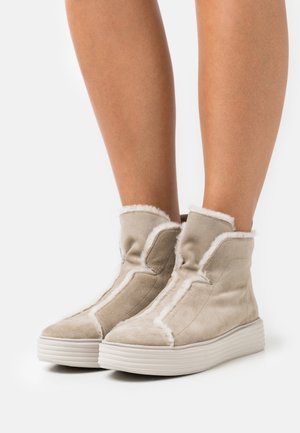 Bottines en suède beige avec une doublure blanche douce, doté d'un bout rond et d'une semelle blanche texturée avec des rainures horizontales.