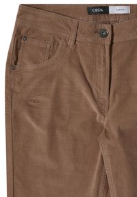 Pantalon en velours côtelé marron avec poches avant, passants de ceinture, fermeture par bouton métallique et étiquette "CECIL PANTS" à l'intérieur de la ceinture.