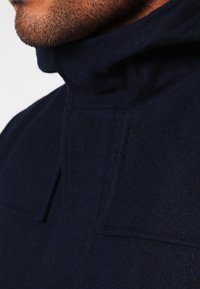 Mörkblå fleecejacka med hög krage, texturerad tyg och minimalistisk design med en enda knappring.